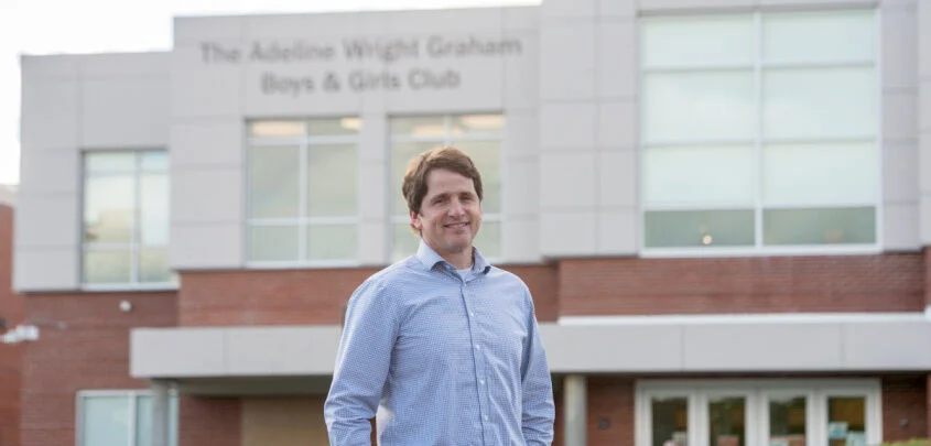 A man standing outside the Adelaide Wright Graham Boys & Girls Club building, smiling, wearing a light blue shirt.