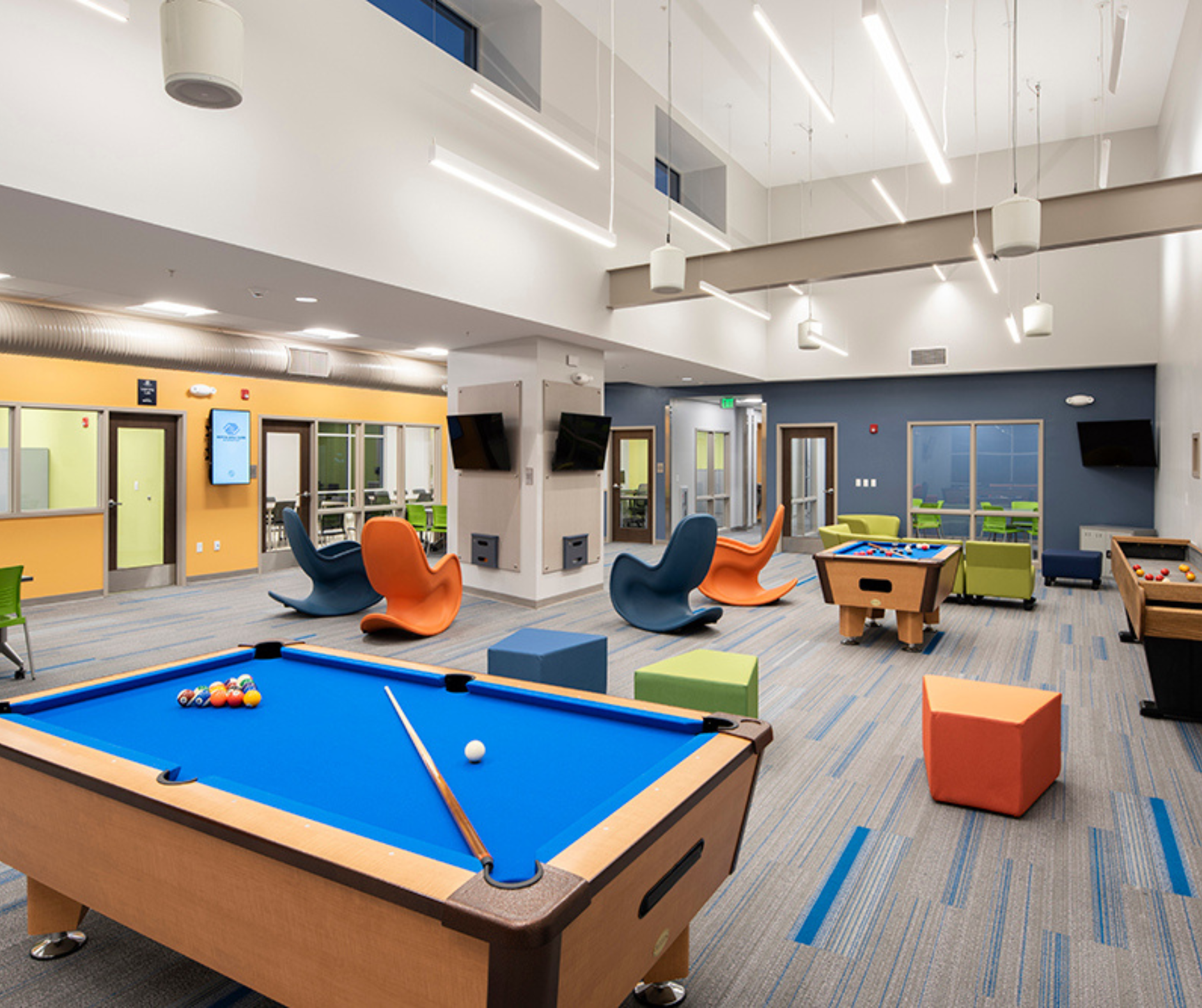 Modern recreational room with pool table, colorful chairs, and gaming area.