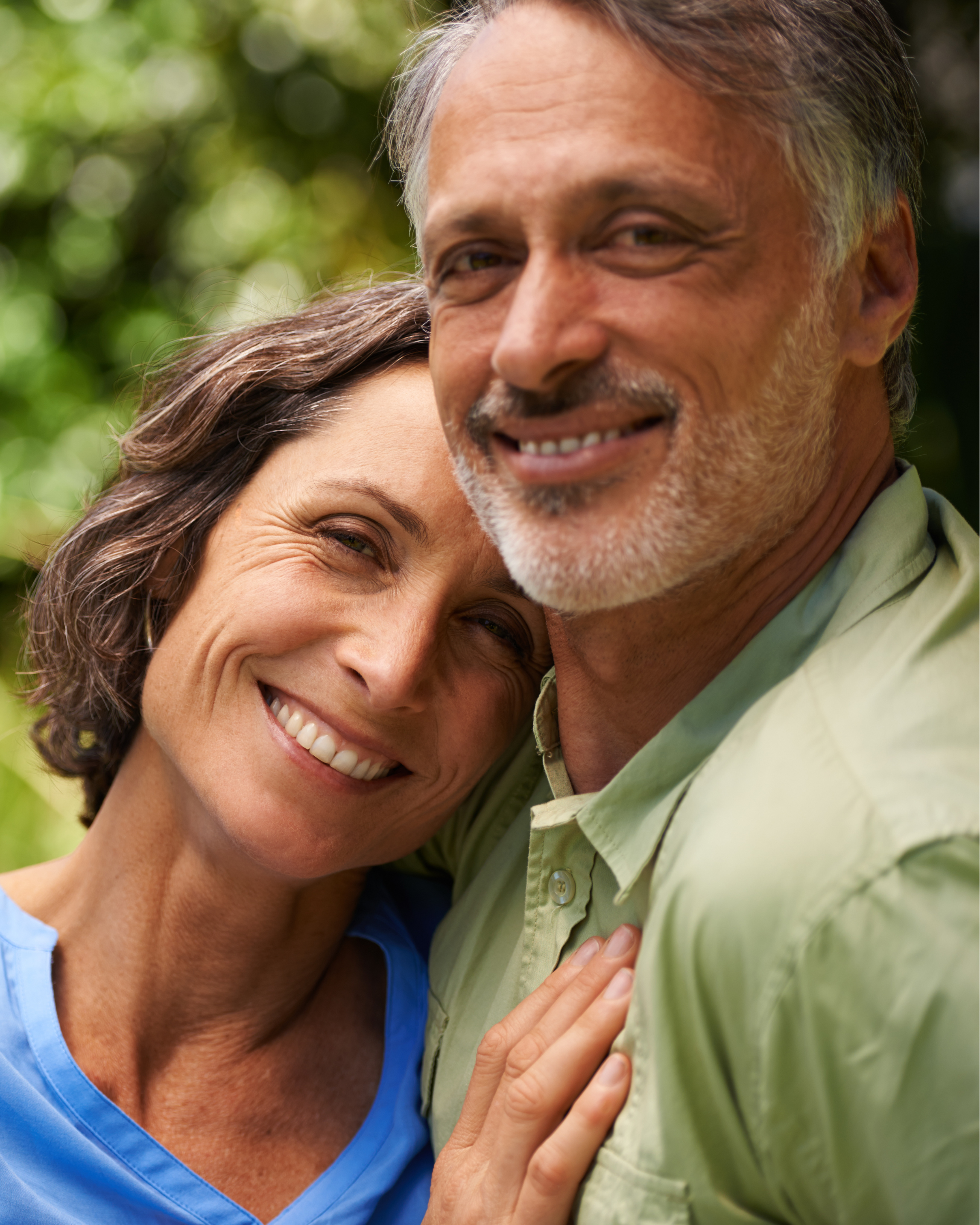 Happy middle-aged couple embracing outdoors with lush green background.