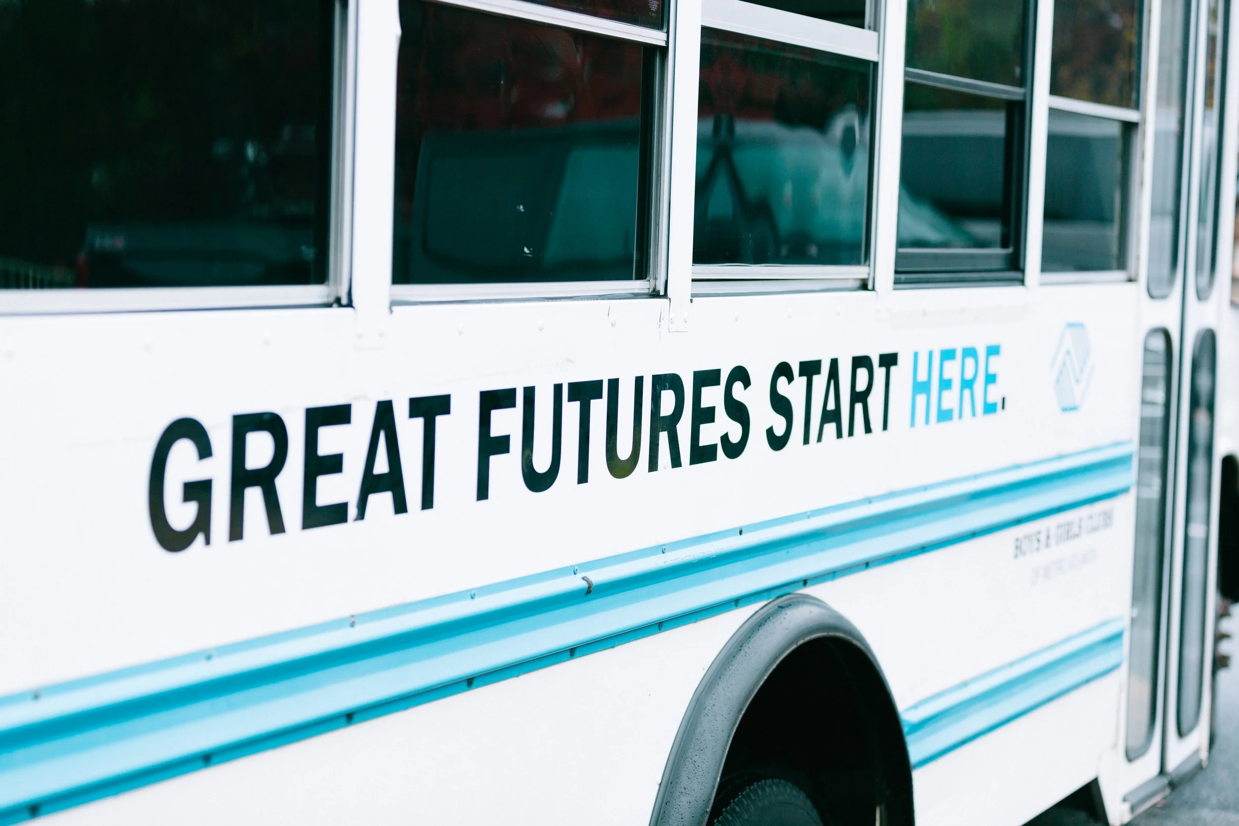A white bus with blue stripes displaying the message 'GREAT FUTURES START HERE' on its side.