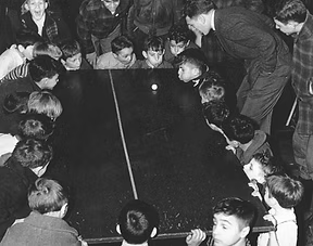 Group of children and adults gathered around a dark pool, possibly participating in a scientific or educational activity.