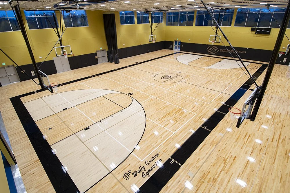 Empty indoor basketball court with yellow walls, black trim, wood flooring, and basketball hoops.