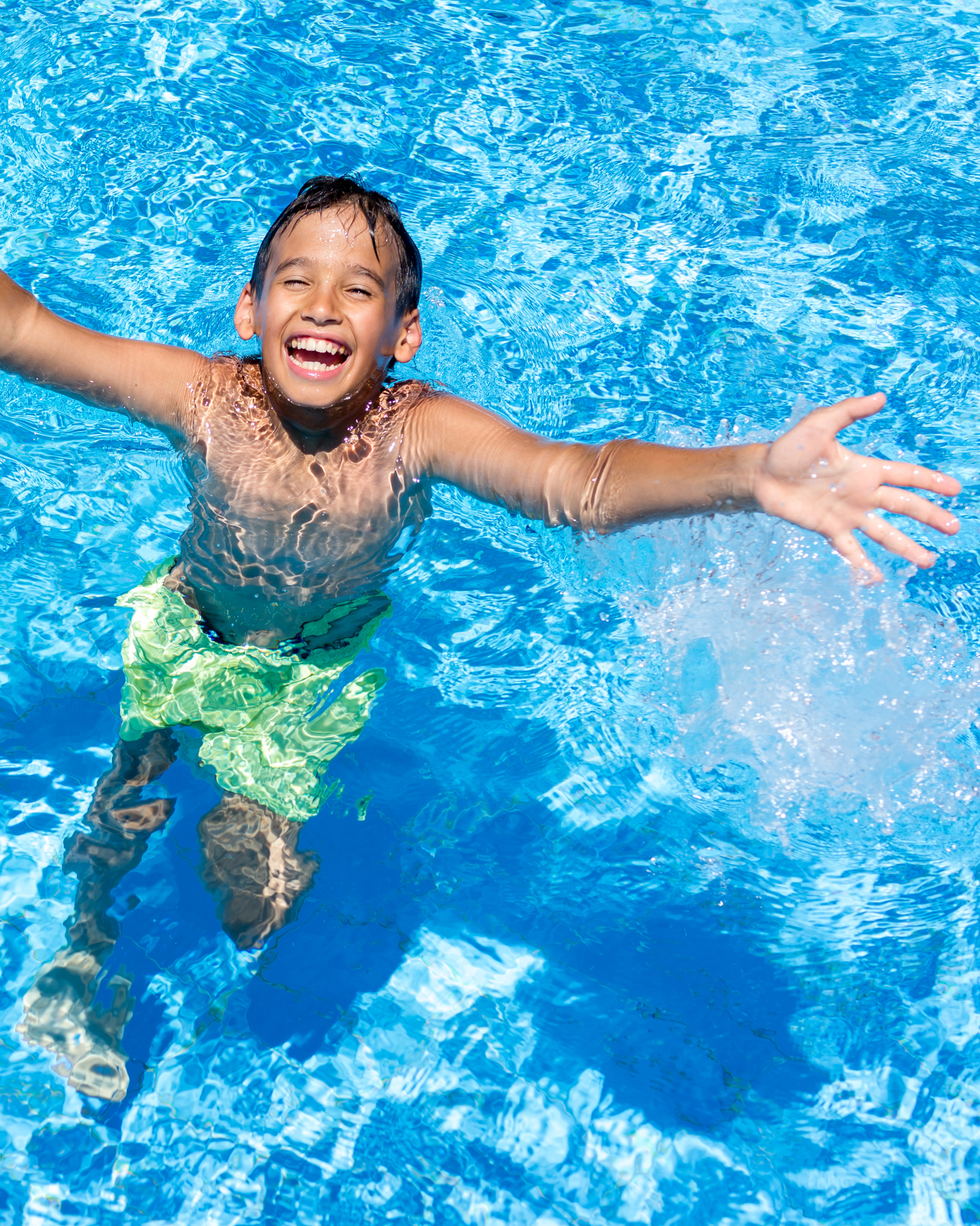 Young boy smiling and reaching out while playing in a swimming pool.