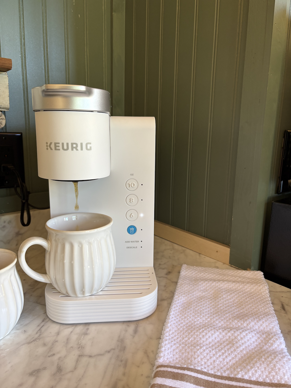 keurig coffee maker with a ceramic mug on the drip tray, set on a marble countertop next to a folded pink towel.