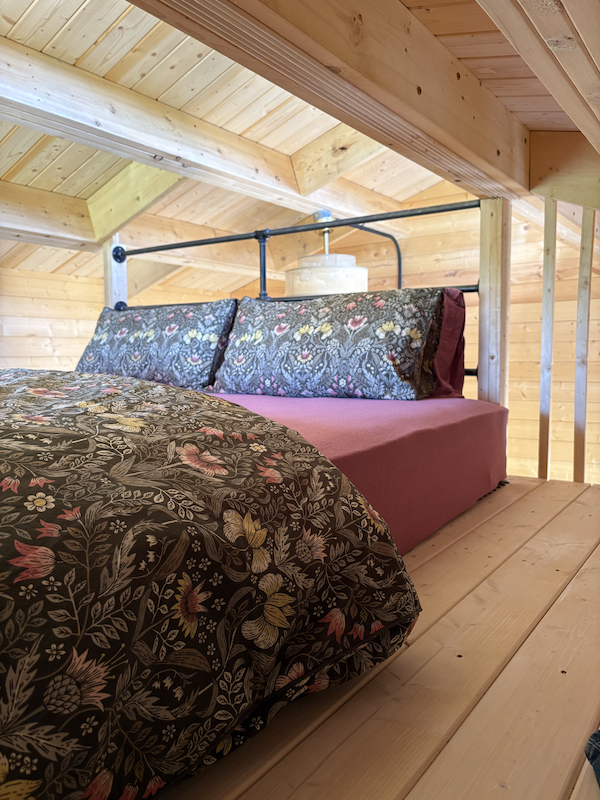 A bed with floral bedding and multiple pillows in a wooden cabin loft with sloped ceiling.