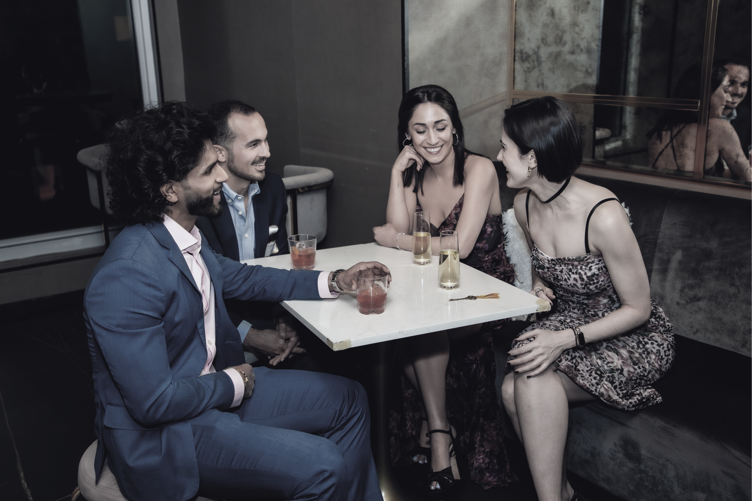 Two men and two women chatting, smiling and laughing over cocktails at a singles event