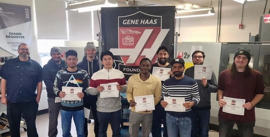 Group of CNC students holding scholarship certificates with Gene Haas Foundation logo on them, and a Gene Haas Foundation banner behind them.