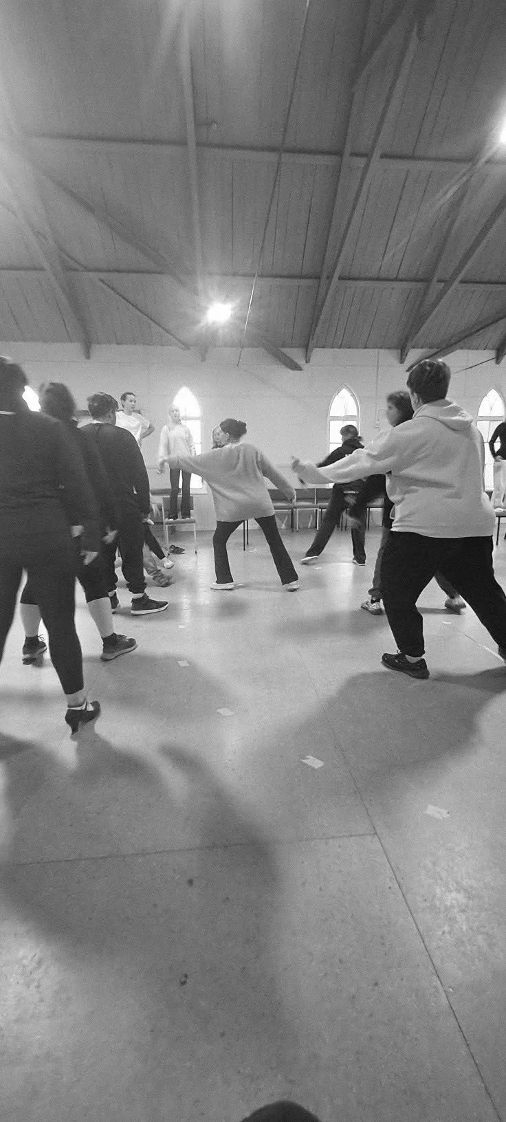 People dancing and practicing together in a large indoor space with high wooden ceiling and arched windows.