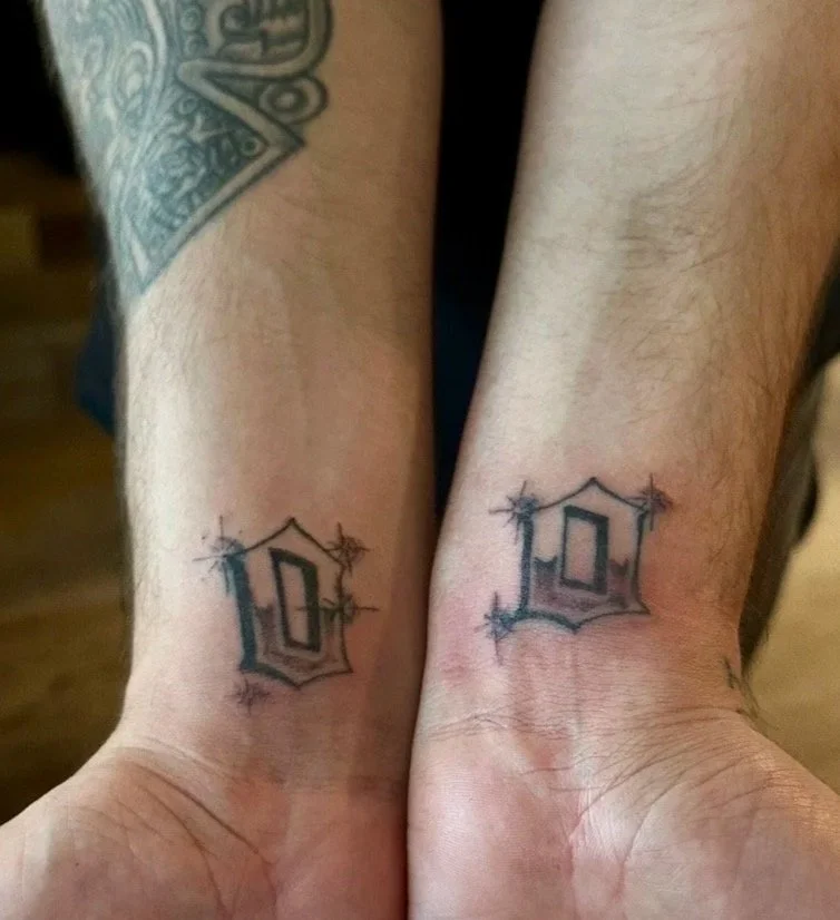 Two wrists with matching tattoos of black outlined 3D-looking diamonds with starburst accents.