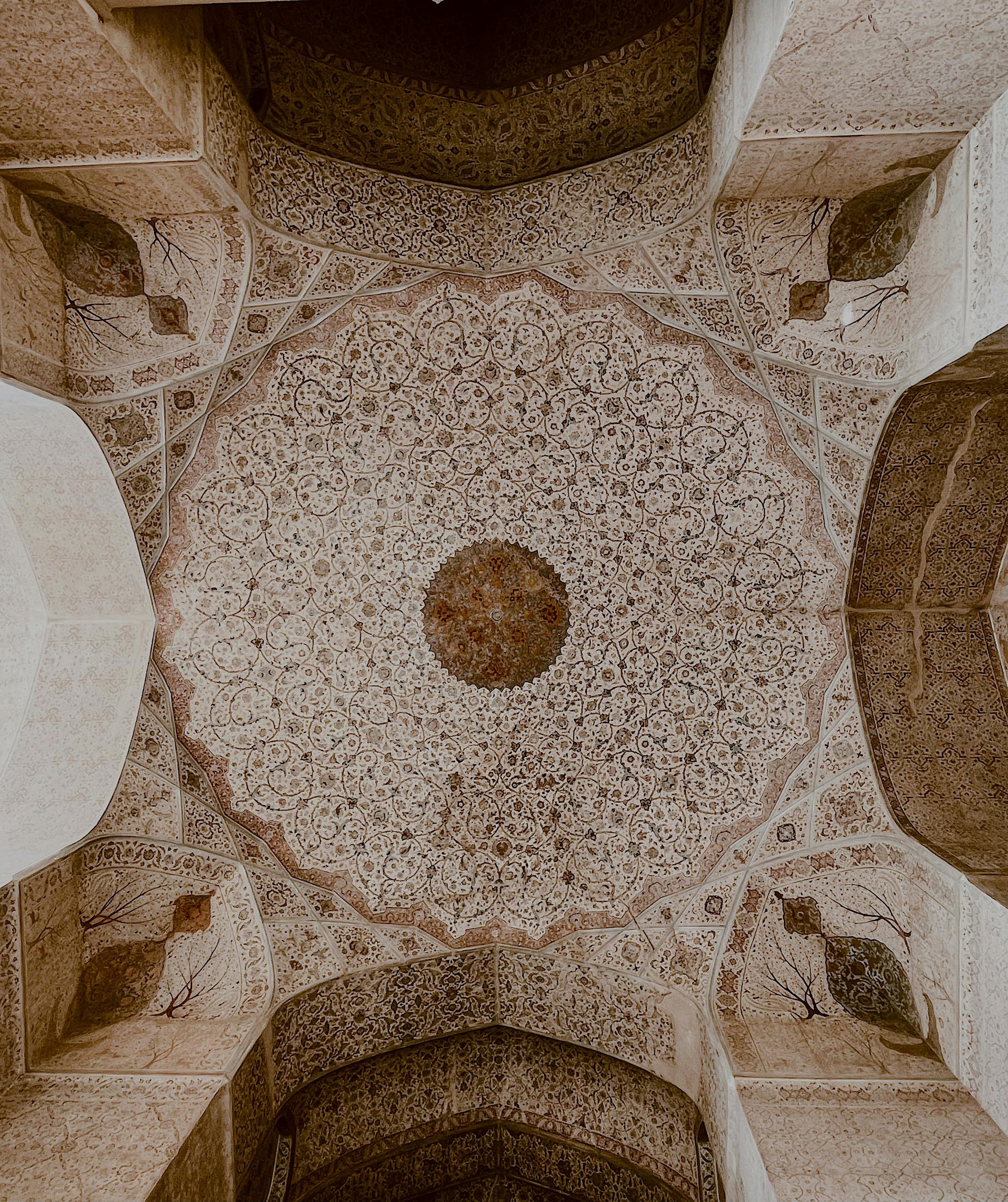 Intricate ceiling mural featuring floral and geometric patterns with a central decorative element, within an archway of an ornate architectural structure.
