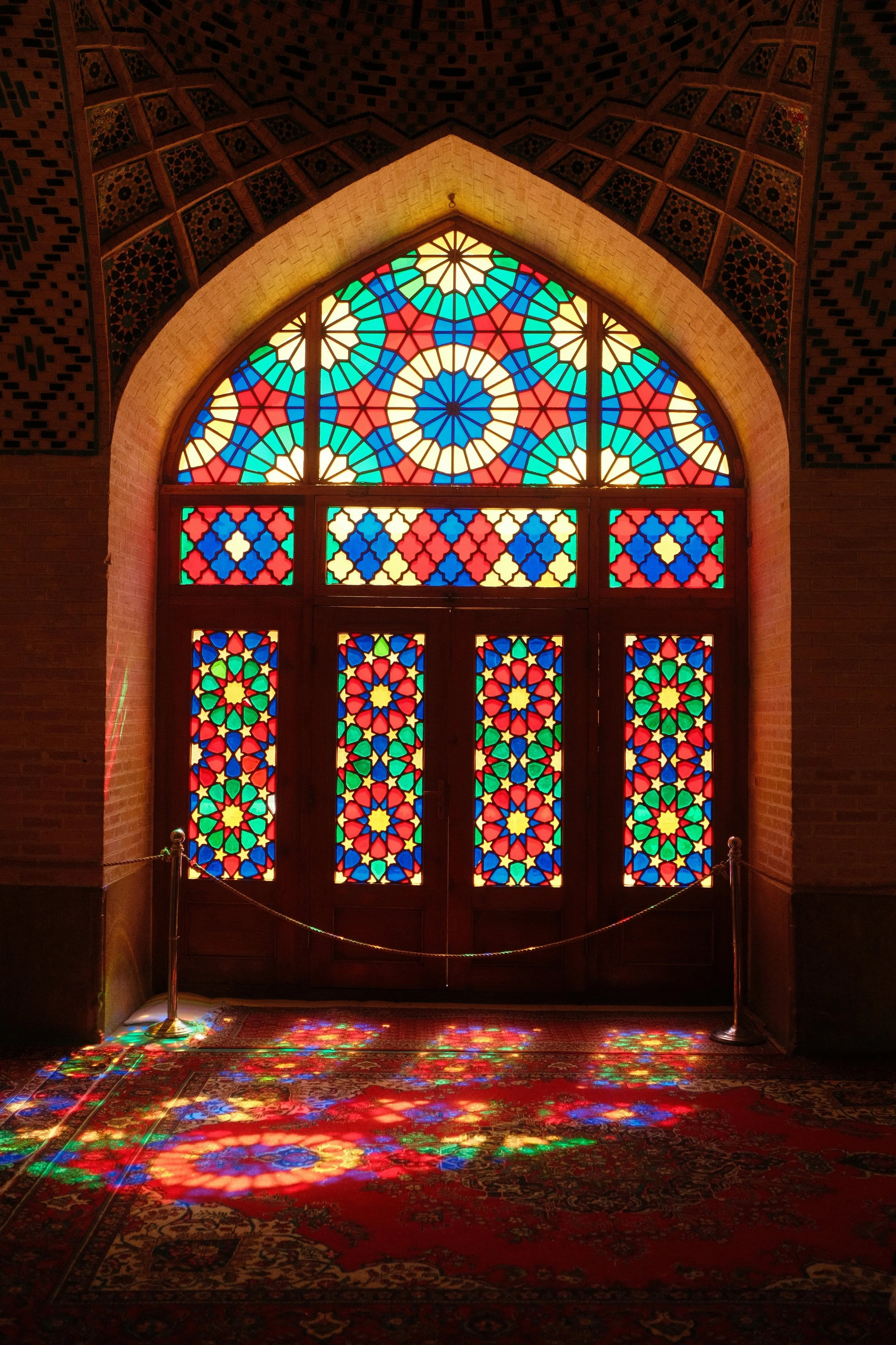 Colorful stained glass window casting rainbow reflections on the floor inside a building with brick walls.