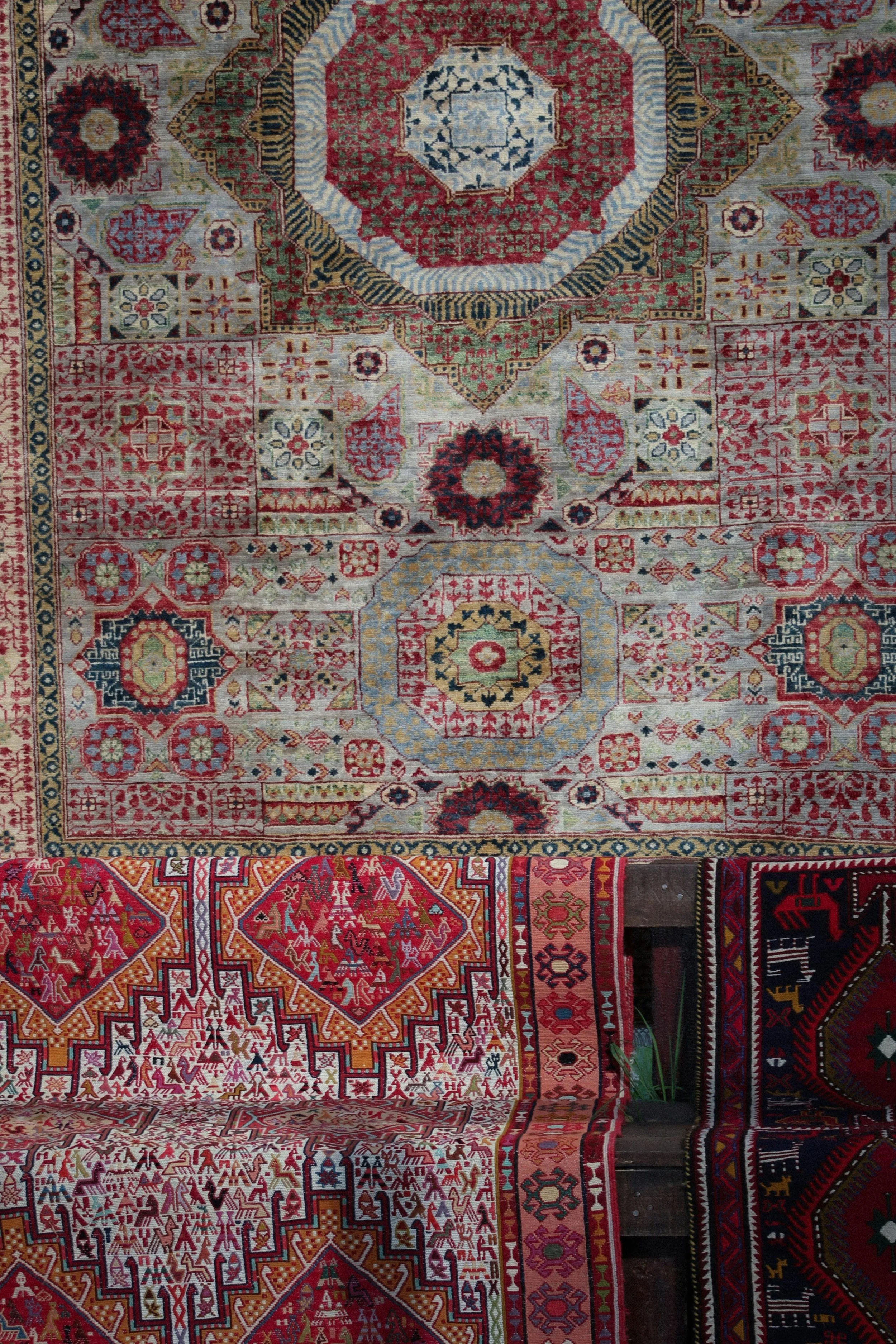 Two Persian-style area rugs with intricate geometric and floral designs, one in red, cream, and black, and the other in cream, beige, and red, layered on a wooden floor.