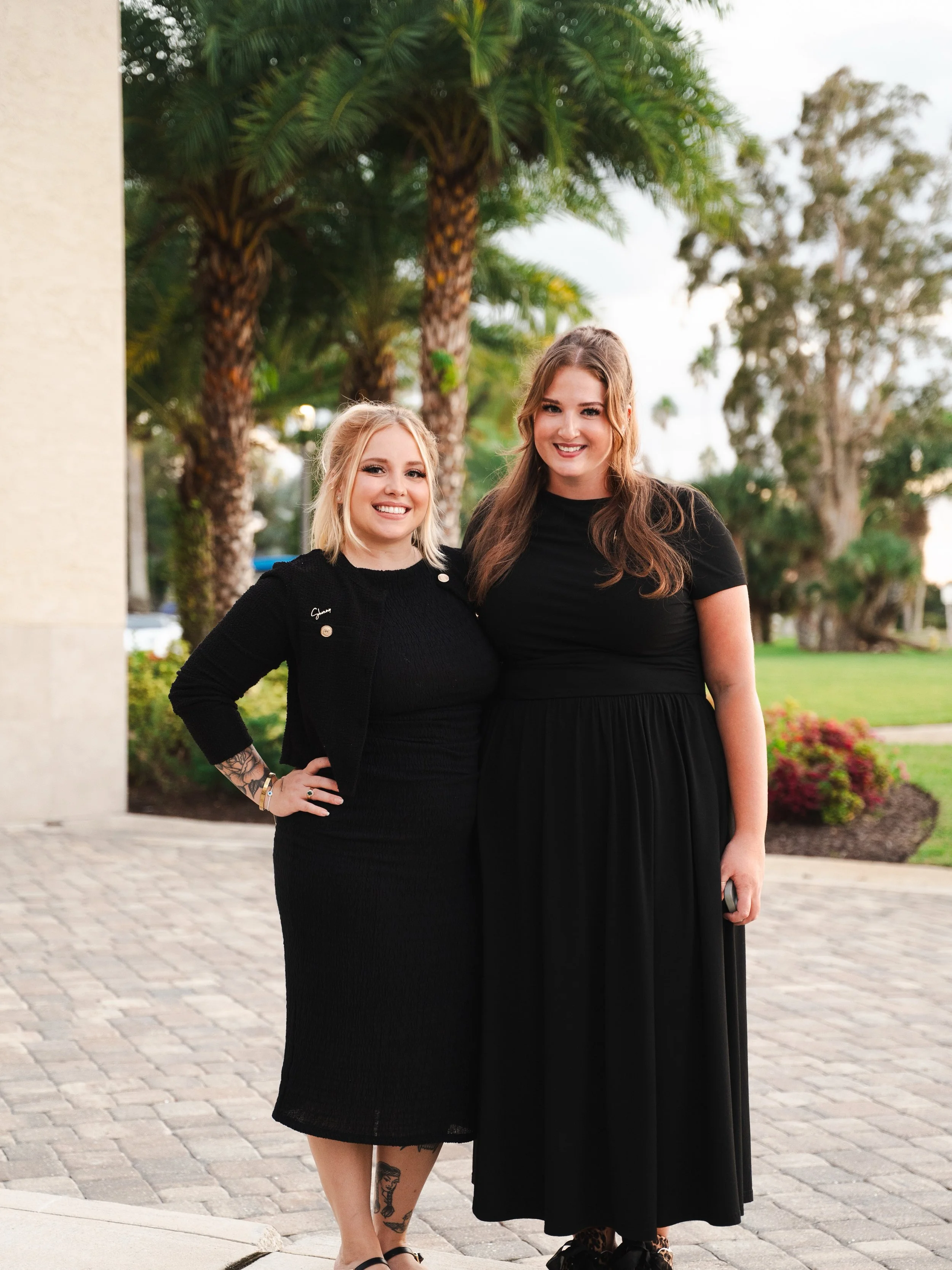 A couple sharing a kiss at their outdoor wedding ceremony, surrounded by bridesmaids in teal dresses holding bouquets, with trees and sunlight in the background.