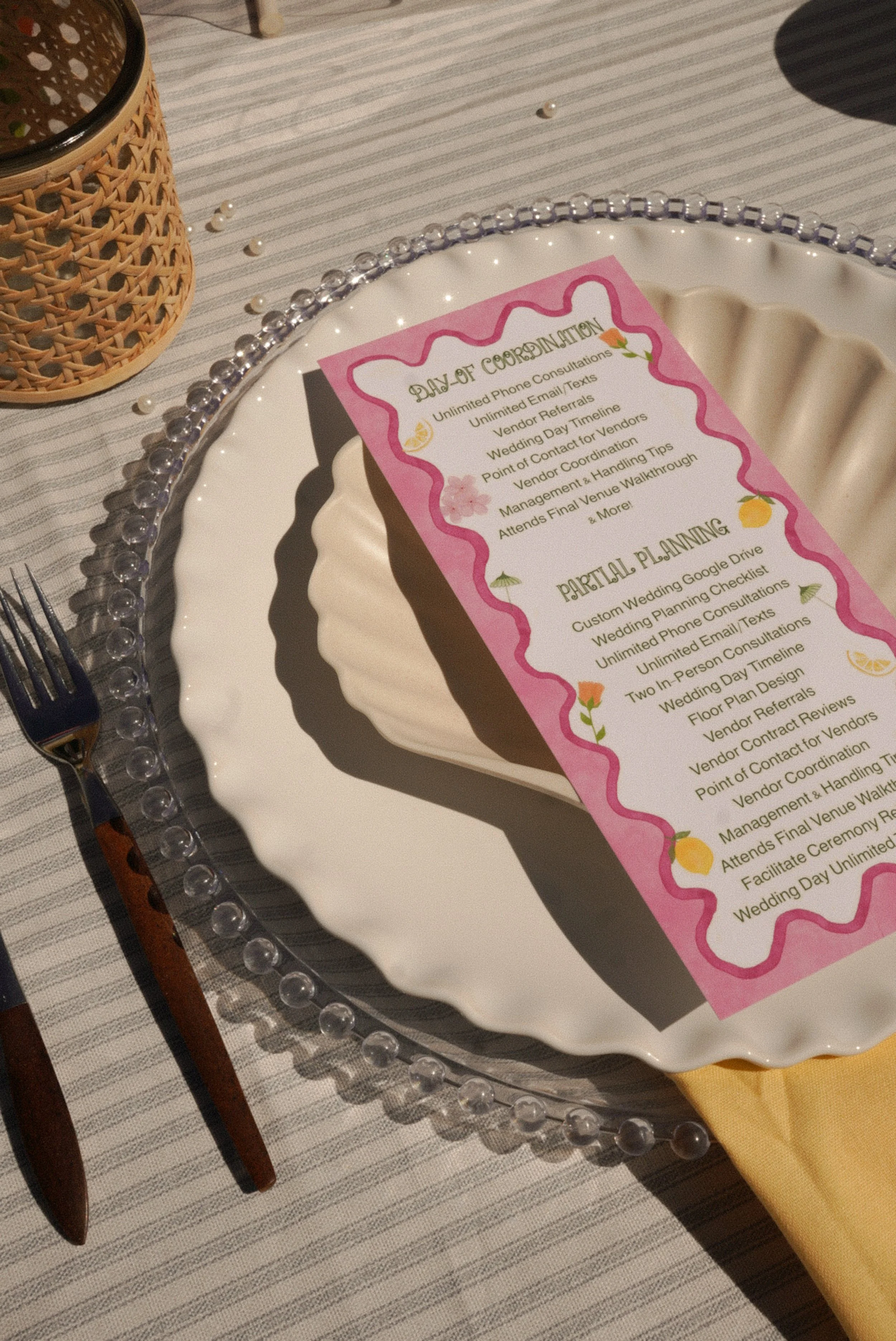 Wedding reception table setting with a decorative plate, a fork and knife, a yellow napkin, and a menu card with a pink border and floral decorations.