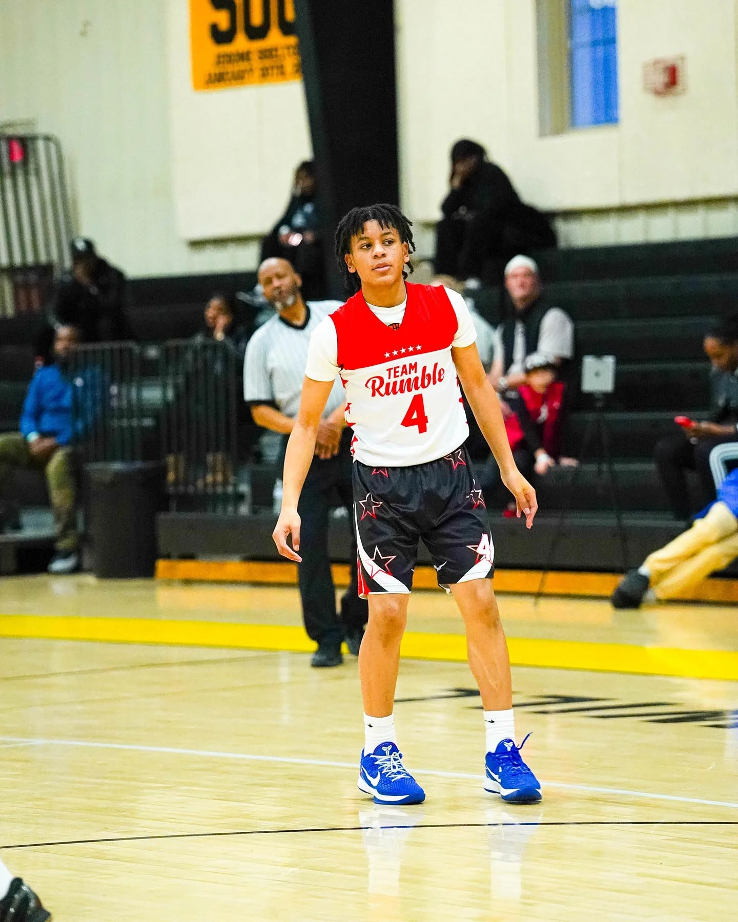 Young basketball player wearing a red and white Team Rumble jersey with the number 4, standing on a gym court during a game.