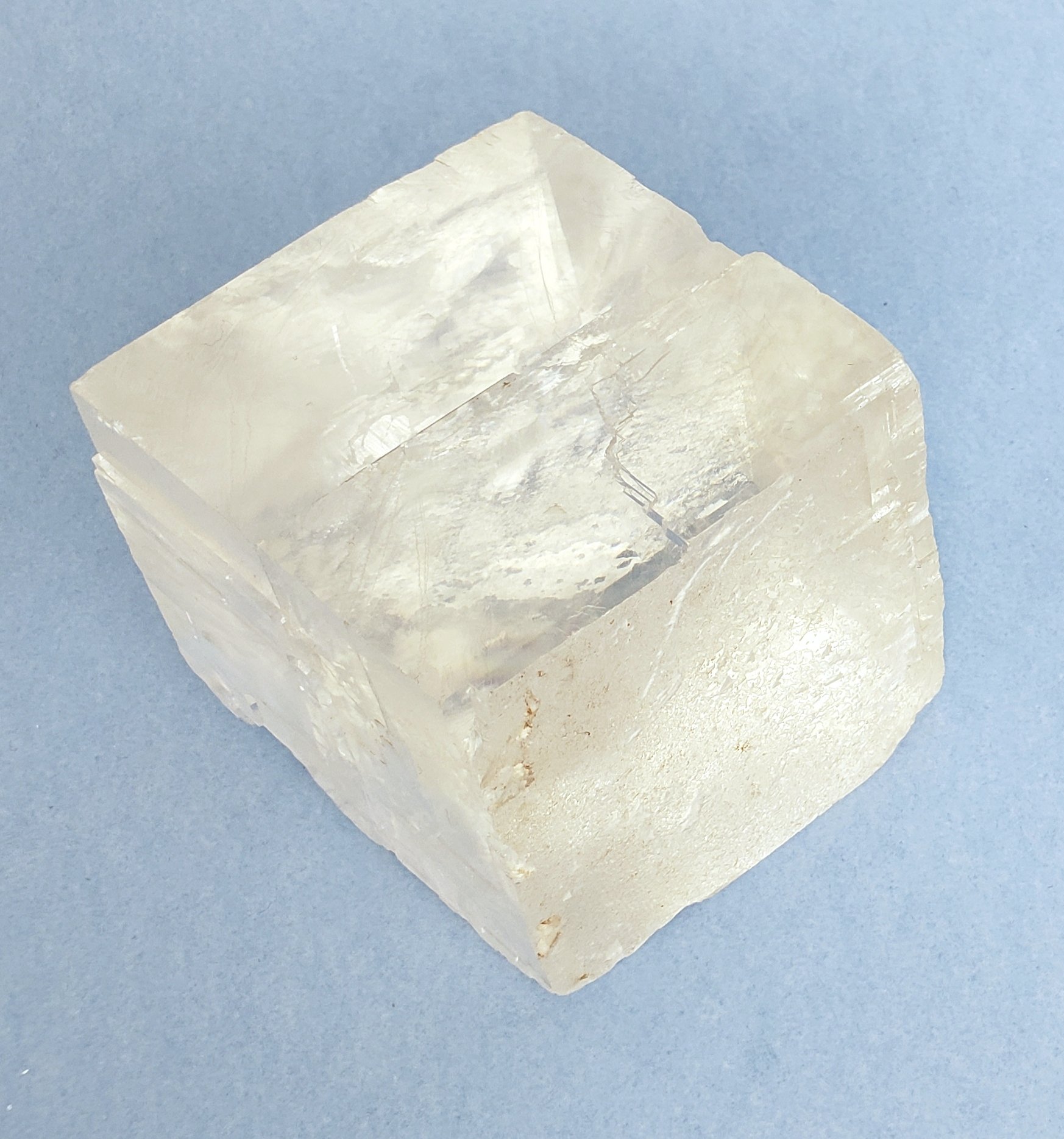 Icelandic Spar. Optical calcite. A translucent, crystalline salt cube on a light blue surface.