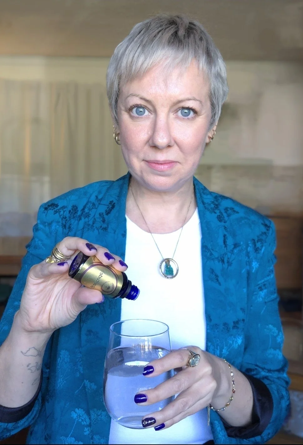 woman, blonde short hair, blue jacket, holding glass bottle over glass of water