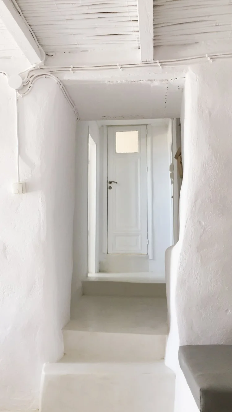 White door at the top of a small set of stairs in a narrow, white-walled hallway.