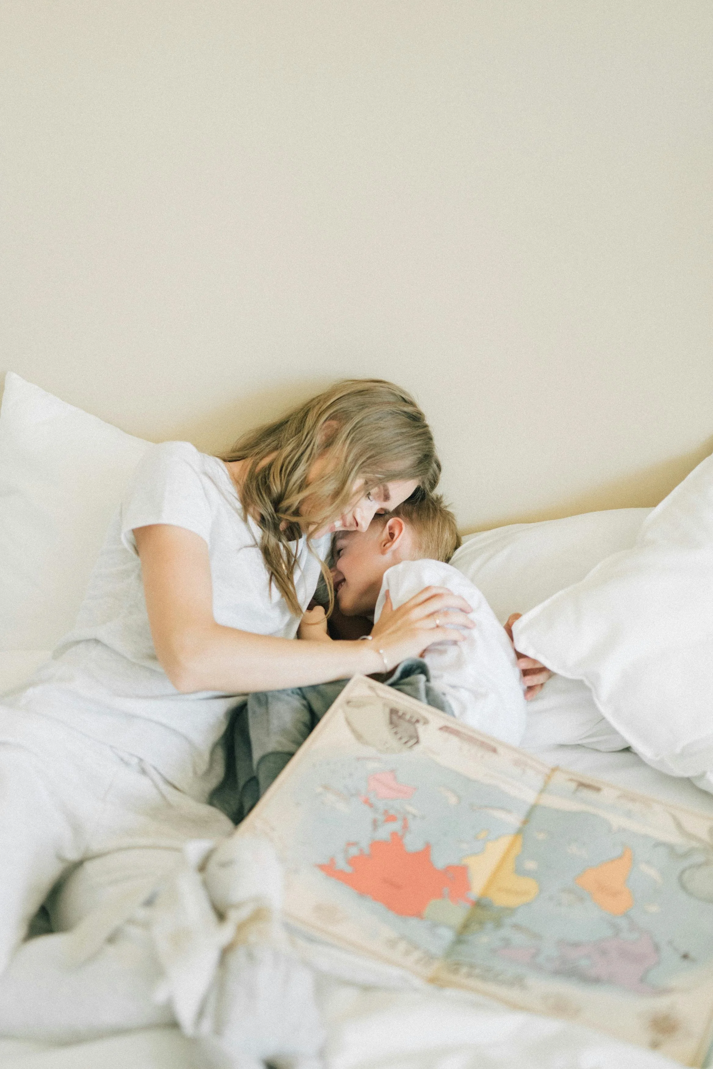 A woman and a young boy are lying on a bed, cuddling and smiling at each other, with a world map in front of them.