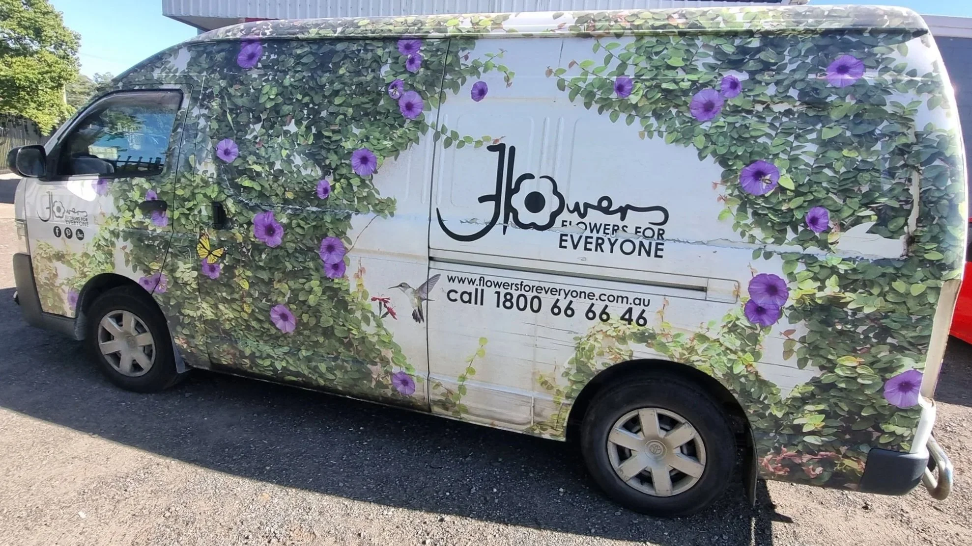 A white van decorated with a vibrant wrap of green leaves and purple flowers, promoting 'Flowers for Everyone'; includes website and contact information.