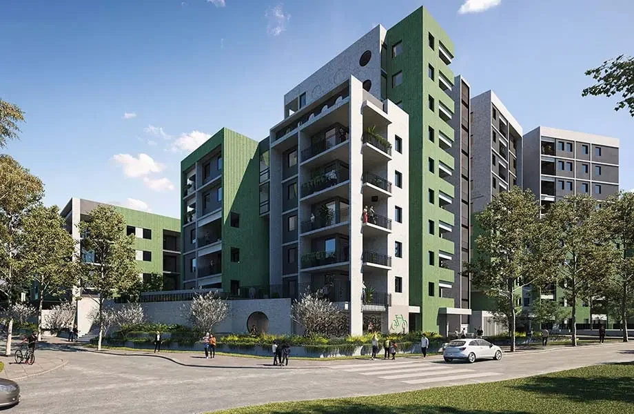 Modern multi-story apartment complex with green, gray, and white exteriors, surrounded by trees and people walking on the sidewalk.