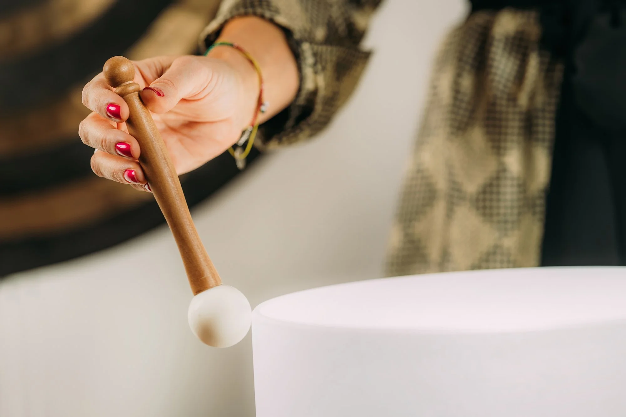 Person playing a white, minimalist singing bowl with a wooden mallet.