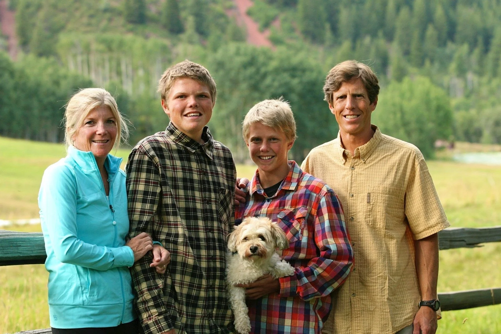 Family of four and a small dog posing outdoors with a forest background.