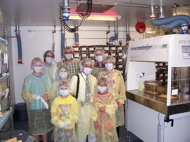Group of people in lab coats and hairnets standing in a cleanroom environment.