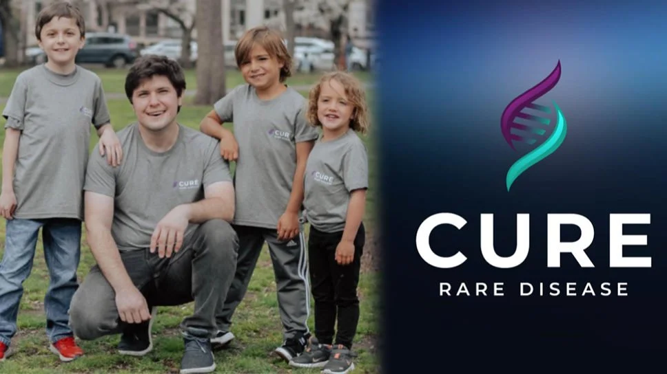Group of people wearing gray shirts with 'CURE' written, standing in a park, next to a logo with a DNA strand and text 'CURE RARE DISEASE' on a blue background.