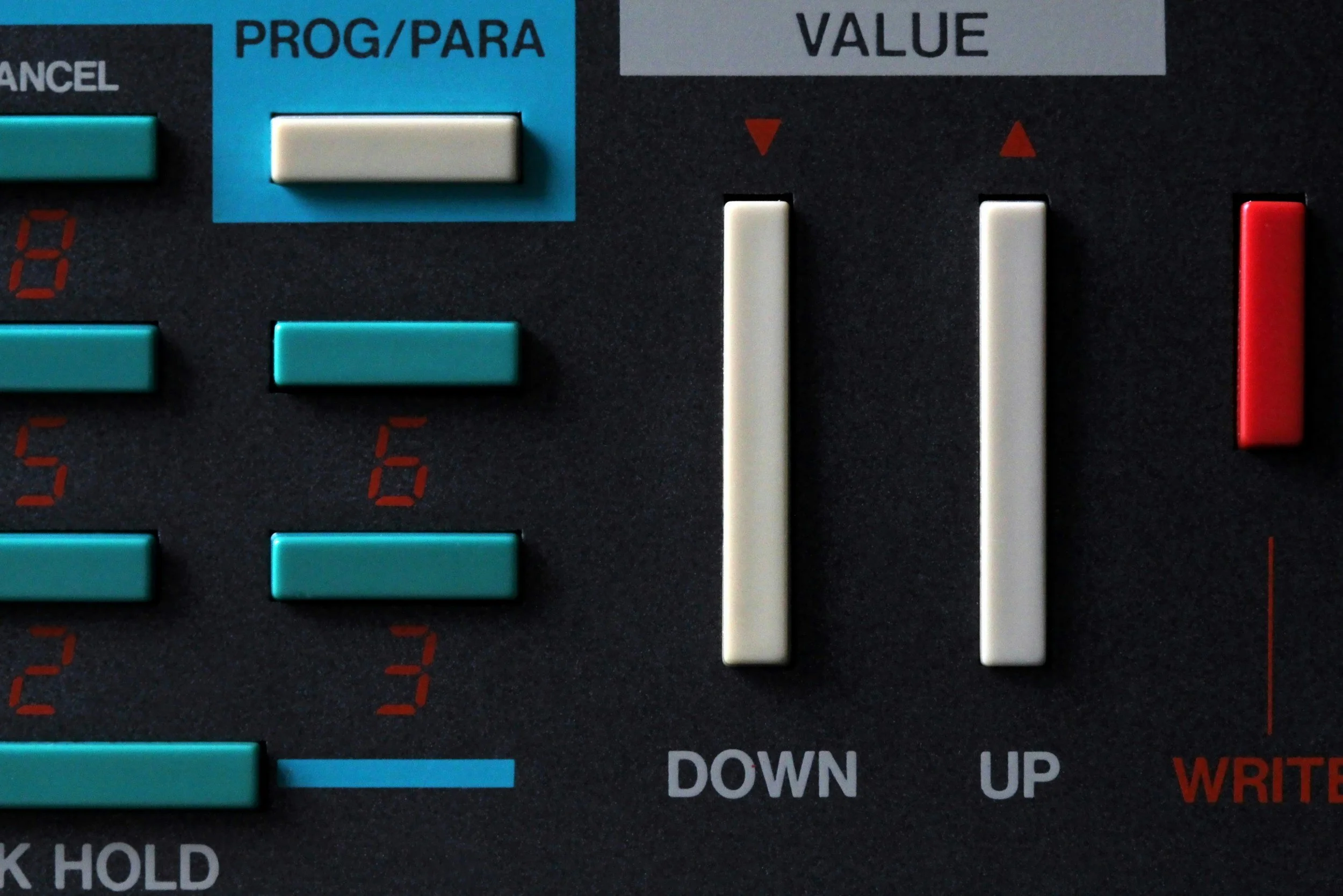 Close-up of a control panel with blue, white, and red buttons and sliders labeled with functions like 'PROG/PARA', 'VALUE', 'DOWN', 'UP', and 'WRITE'.