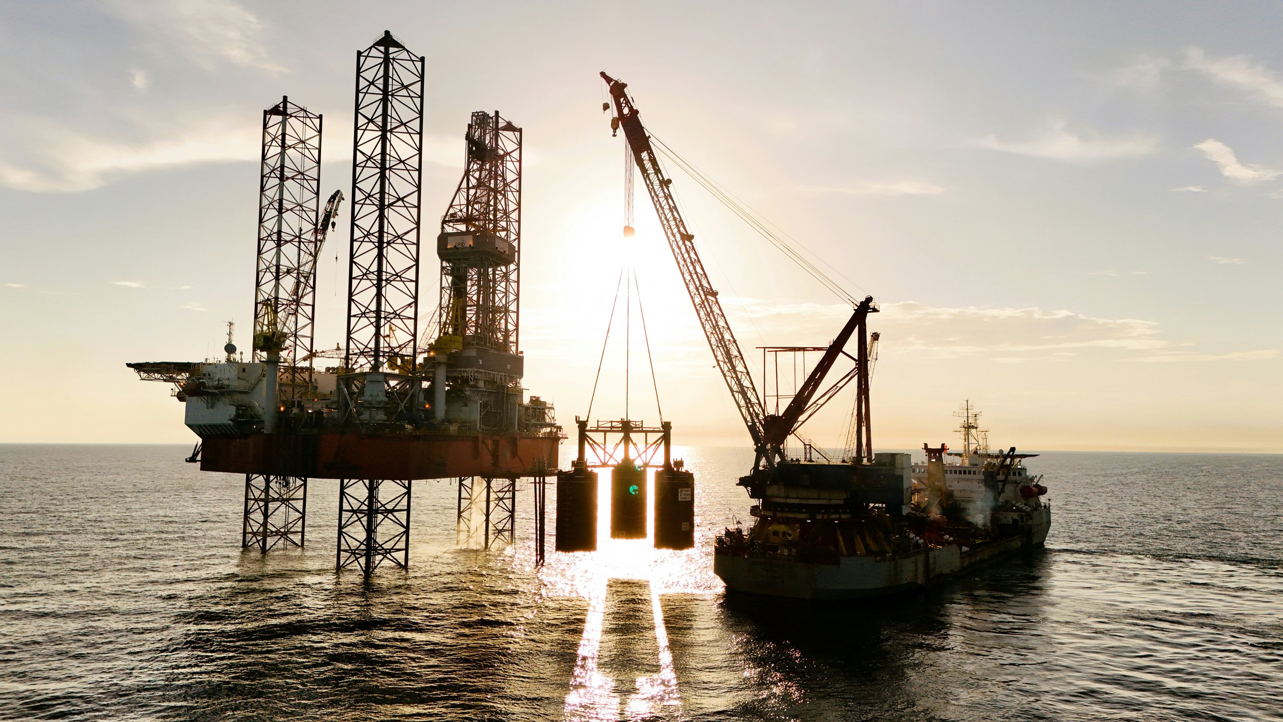 Offshore oil rig drilling platform with cranes during sunset at sea.