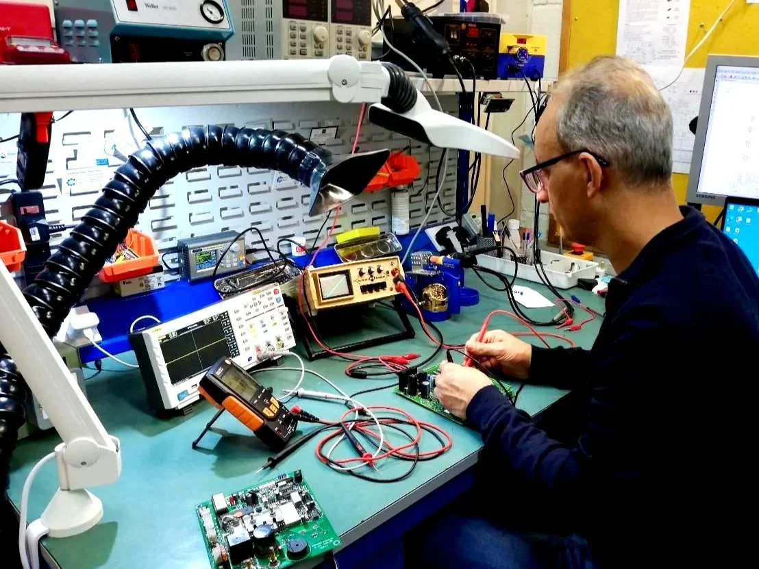 A man working on electronic circuit boards in a workshop with various testing and measuring tools.