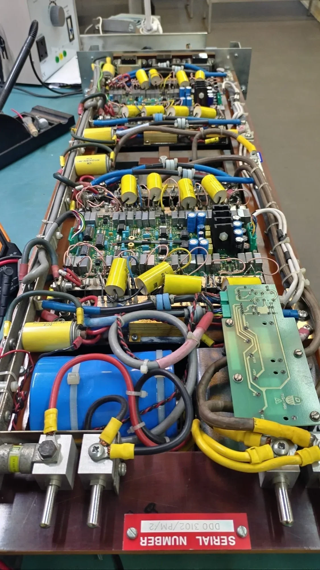 Close-up of an open electrical or electronic circuit board with capacitors, wiring, and other components mounted on a metal frame.