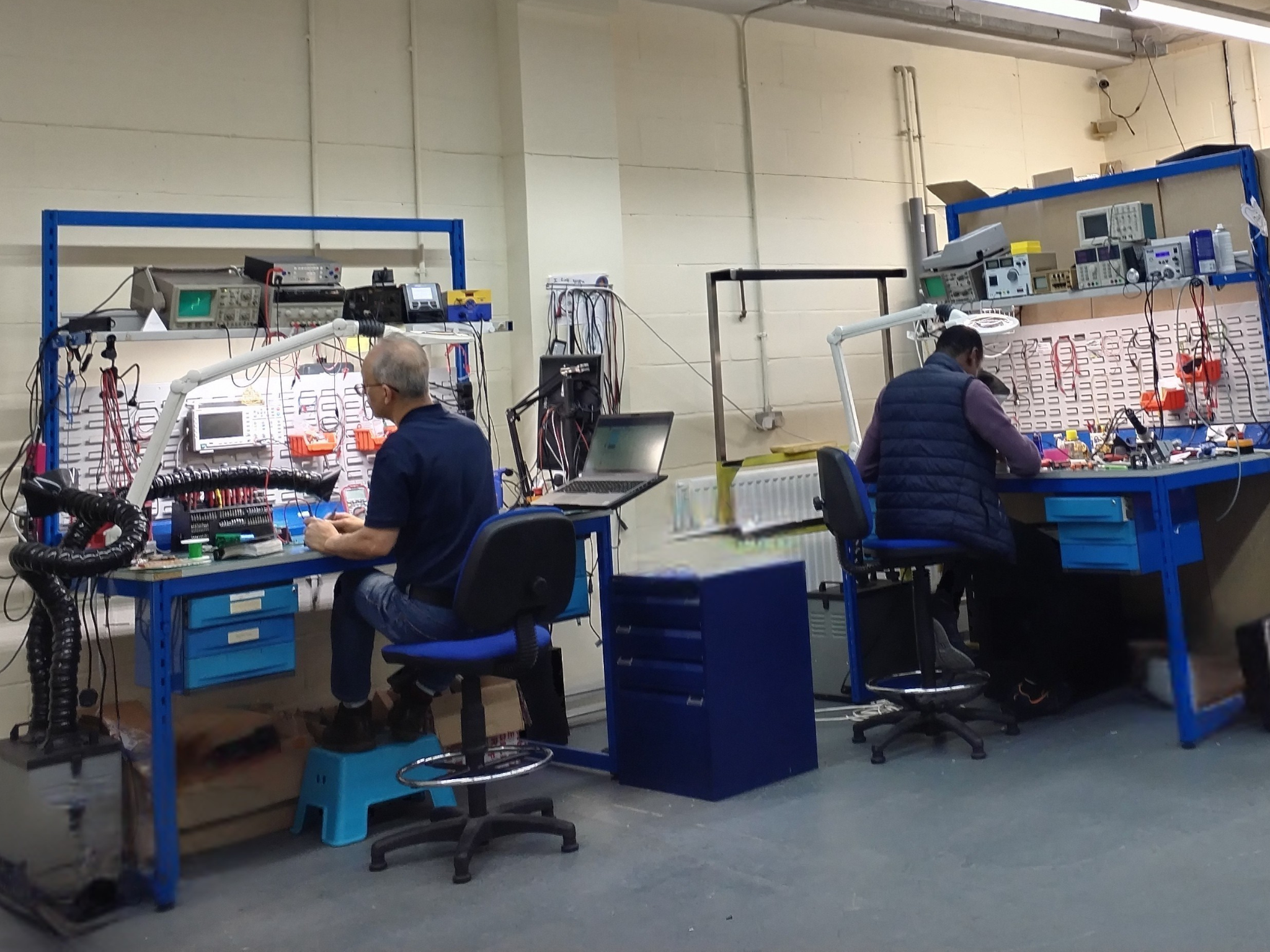 NPE engineers working at electronic repair benches in Newcastle workshop, with test equipment and oscilloscopes