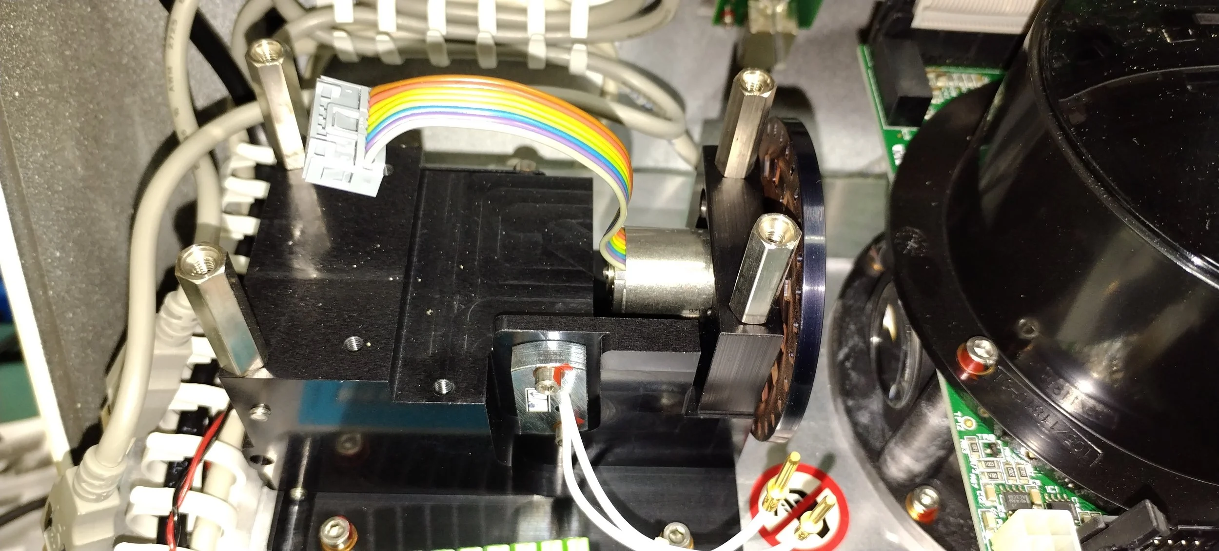 Close-up of electronic components including a black stepper motor, a circuit board, and a multicolored ribbon cable.