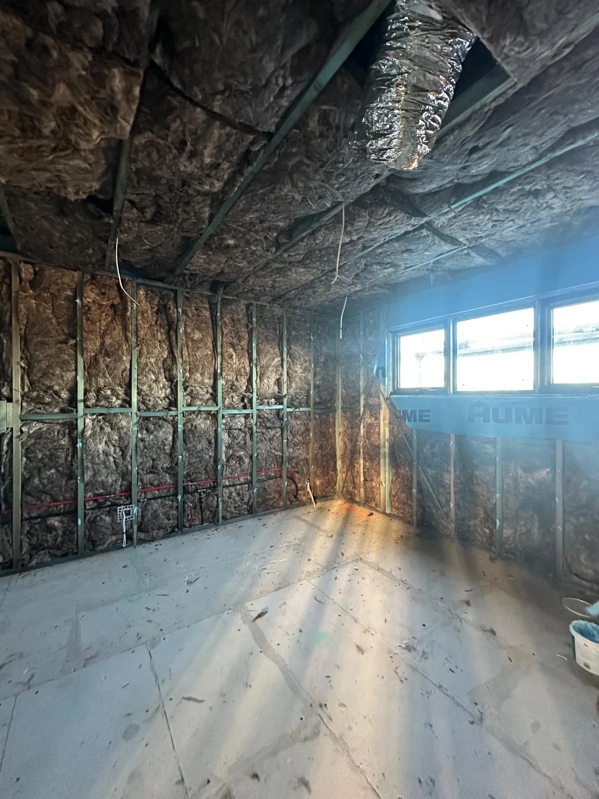 An unfinished room under construction with insulation installed on the walls and ceiling, exposed metal framing, a concrete floor, and a window on the right side.