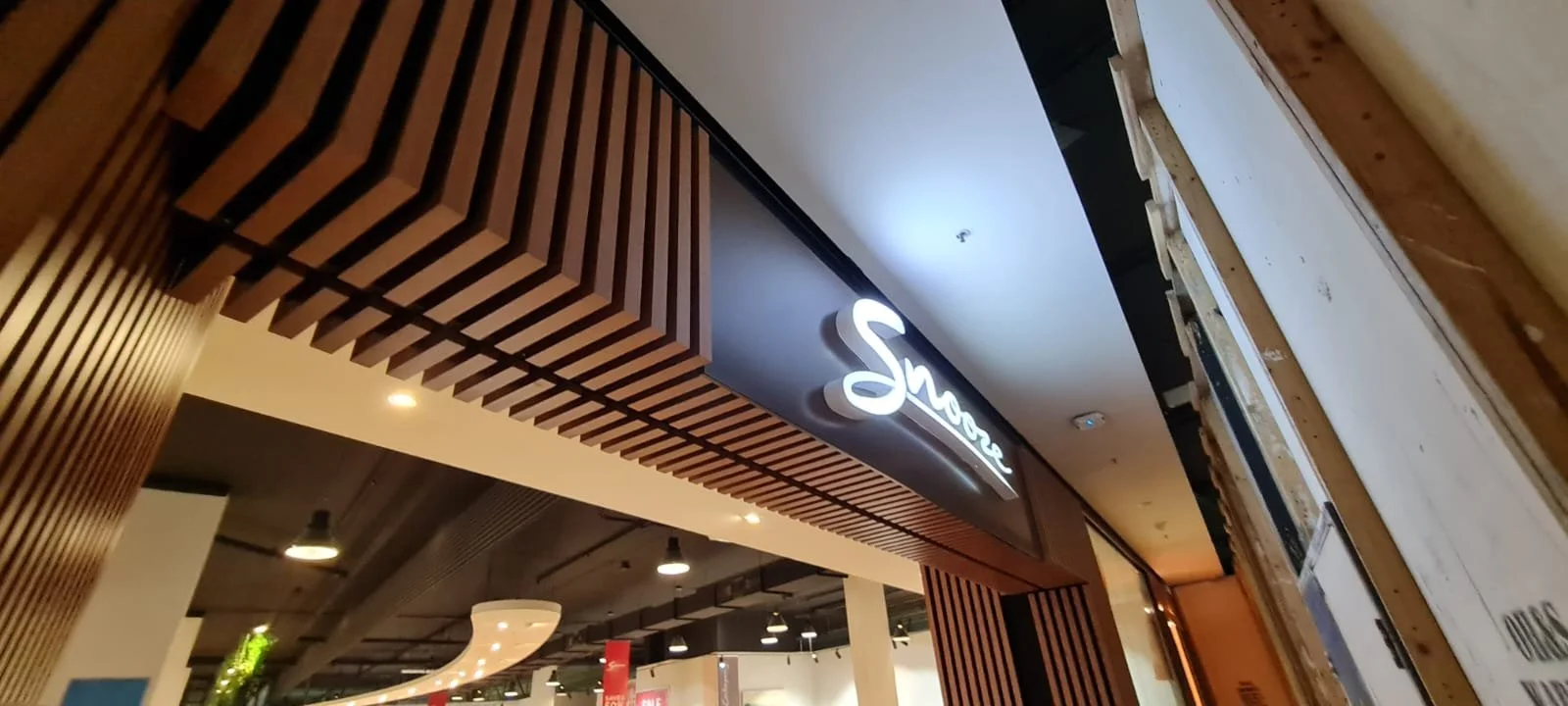 Storefront sign reading 'Smove' inside a mall, with wooden slat design on the ceiling and warm lighting