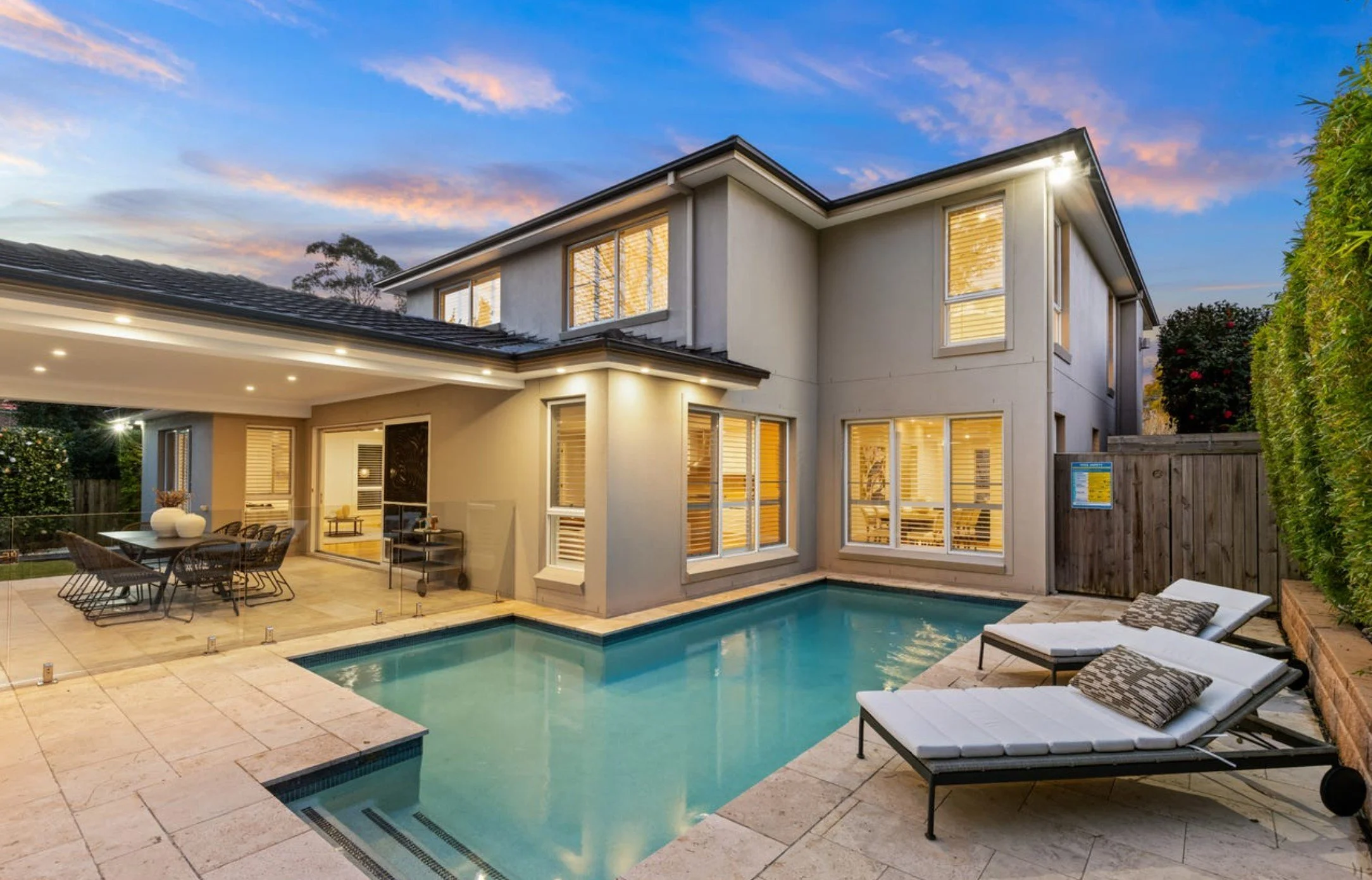 Modern house with large windows, outdoor pool, lounge chairs, and patio dining area at dusk