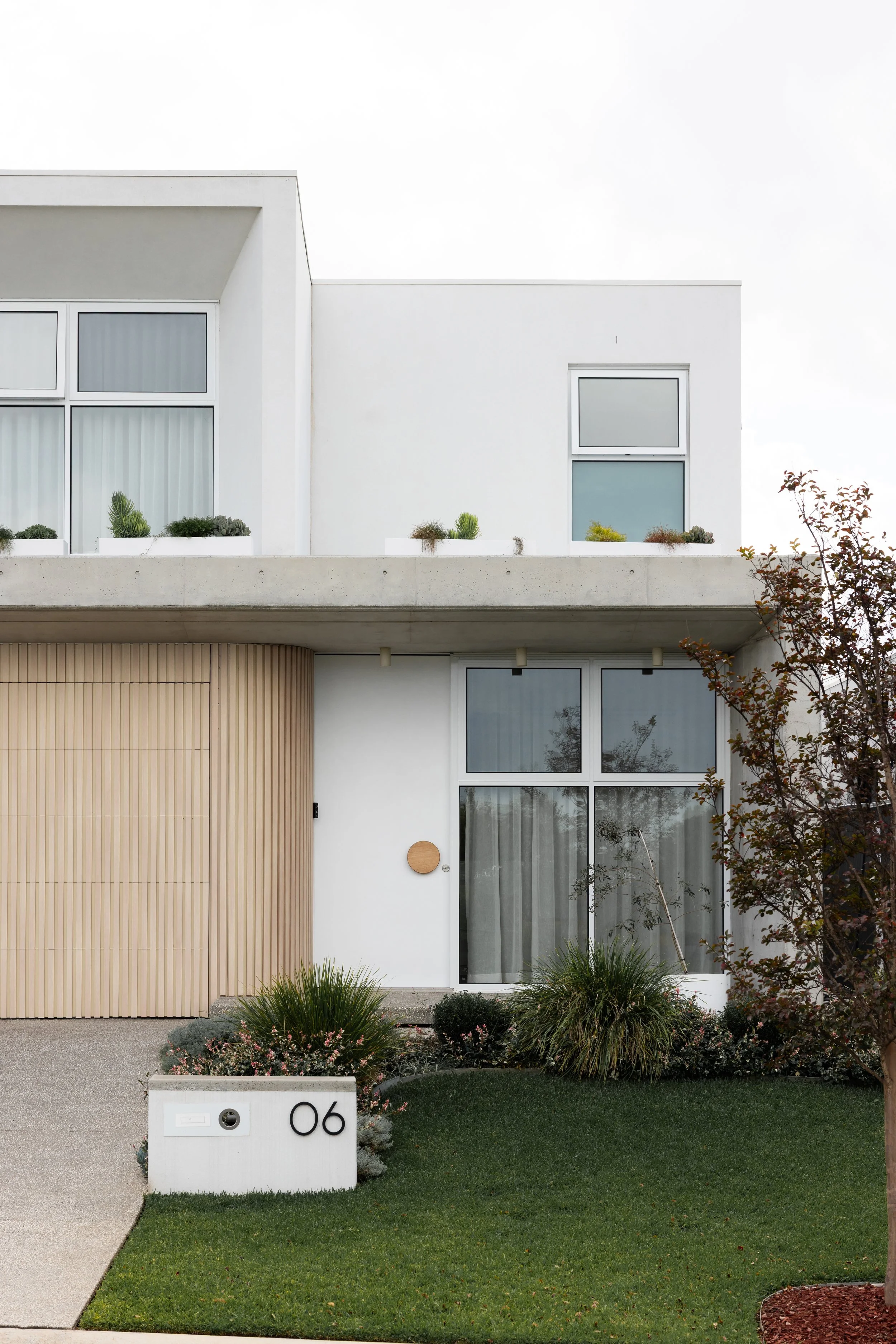 Modern white house with large windows, a small garden, and a house number 06 on a white mailbox in front.