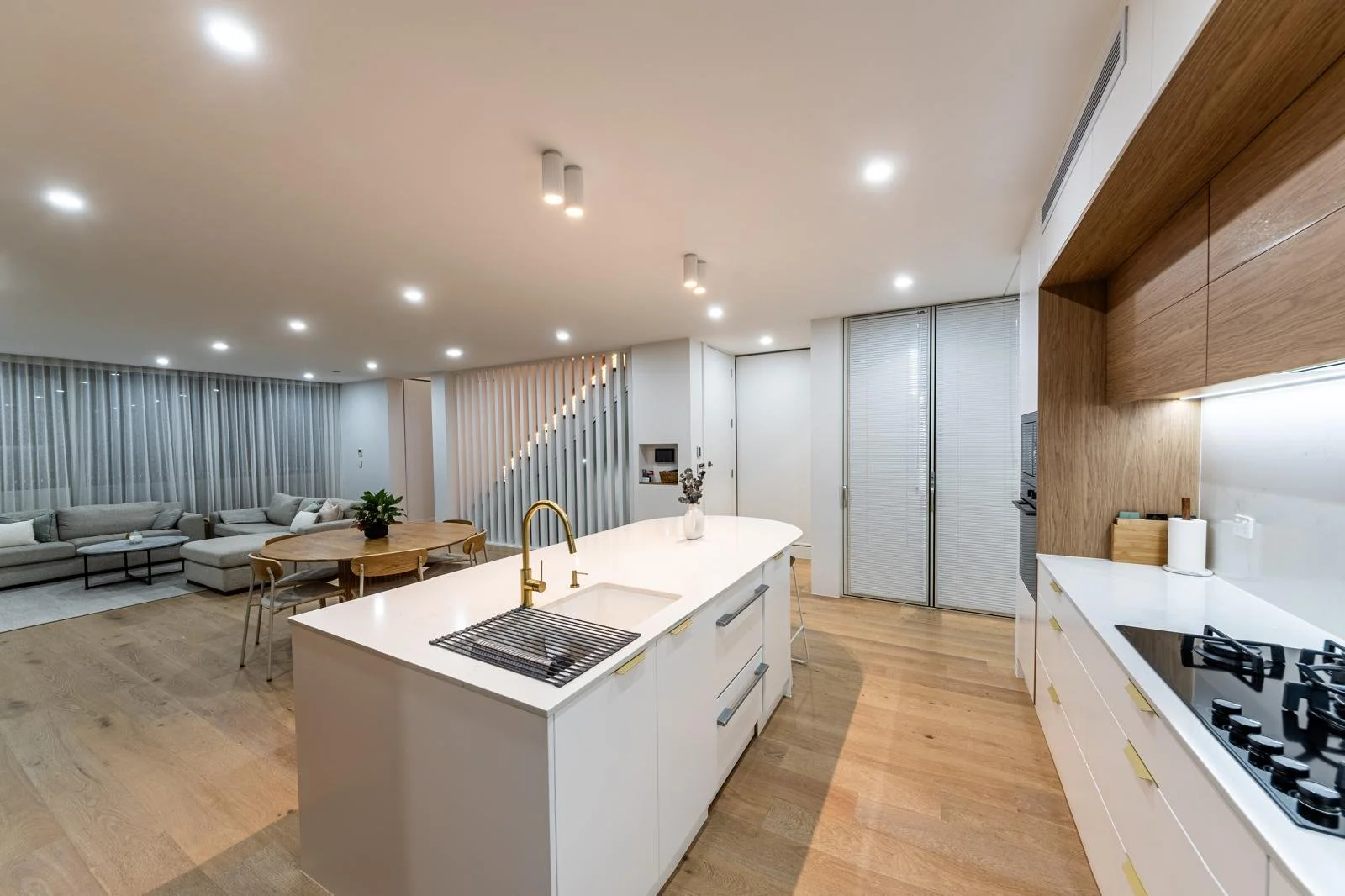 Modern open-concept kitchen and living room with white cabinetry, wooden accents, and plenty of lighting.