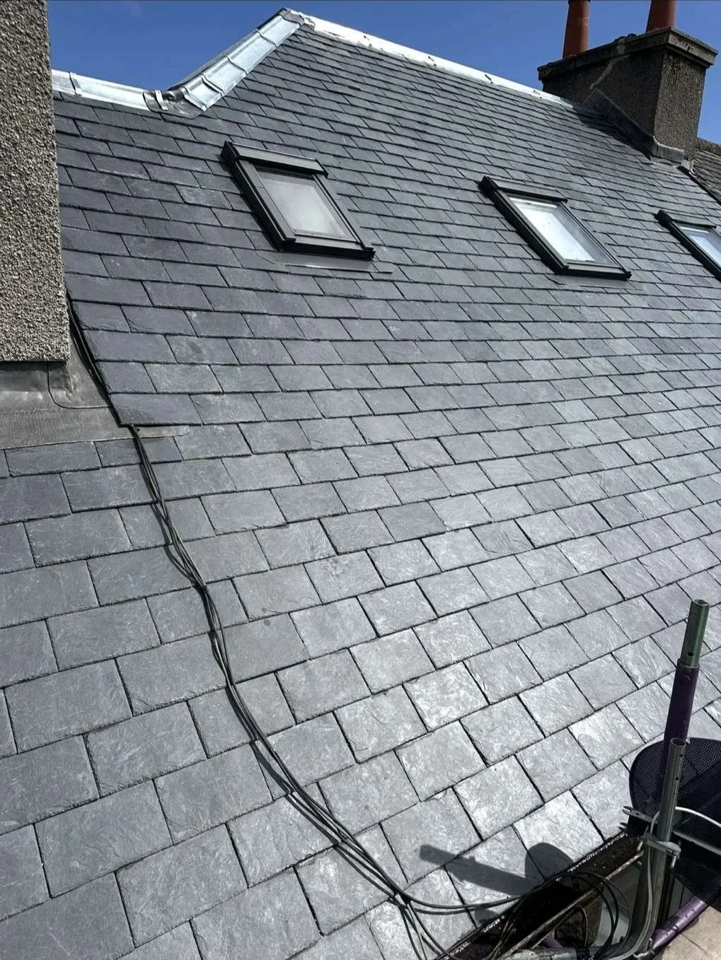 Slate roof with three skylights and visible wiring, under a blue sky.