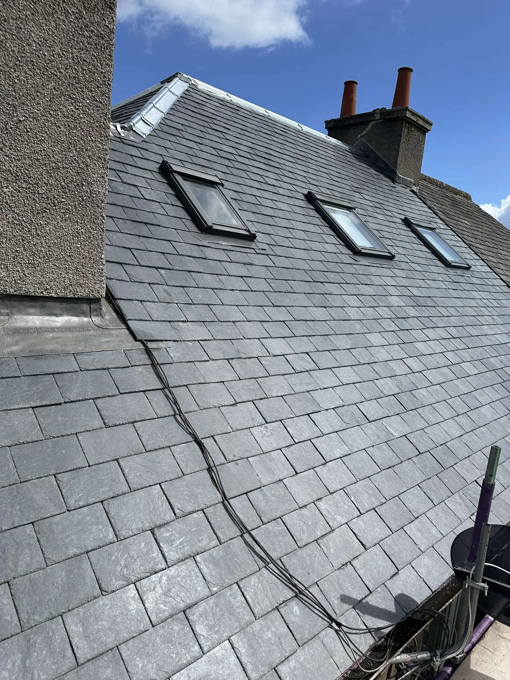 Roof with three skylights, chimney with two red pipes, and electrical wires running down the roof.