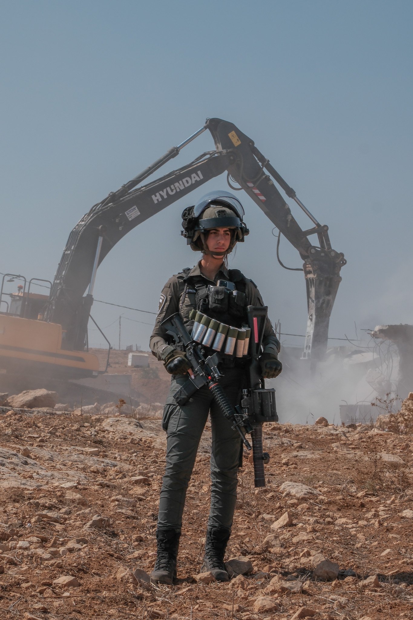 An Israeli soldier stands guard with an assault rifle and tear gas as a Palestinian home is demolished behind her in the occupied village of al Khaldeya.