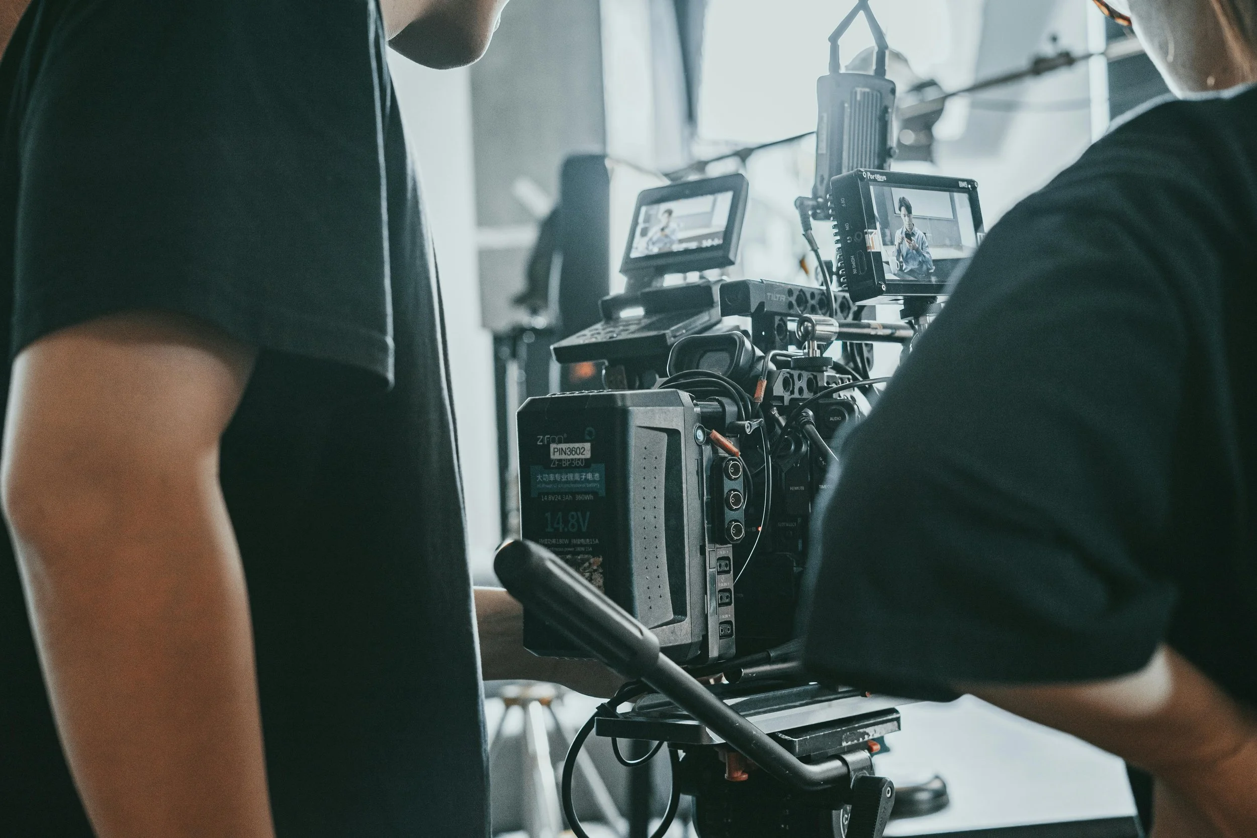 Close-up of a person operating a professional film camera on a film set with another crew member in the background.