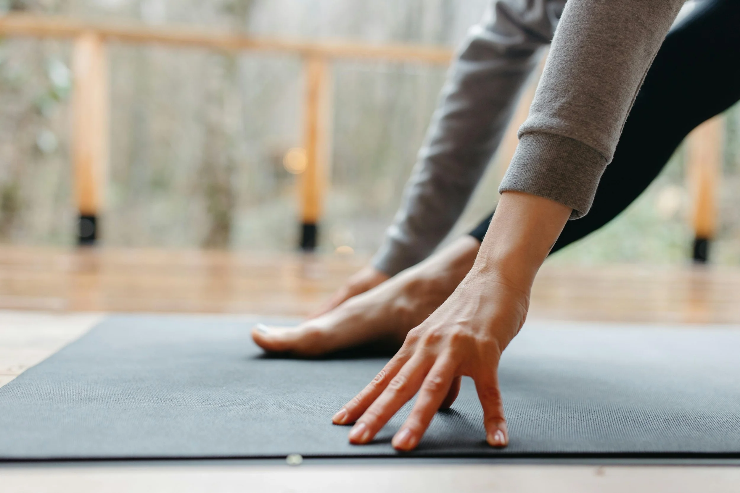 Close-up of person stretching on yoga mat, focusing on hands and arms, indoors with natural light.