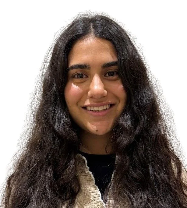 A young woman with long, curly dark hair and tan skin smiling at the camera against a plain white background.