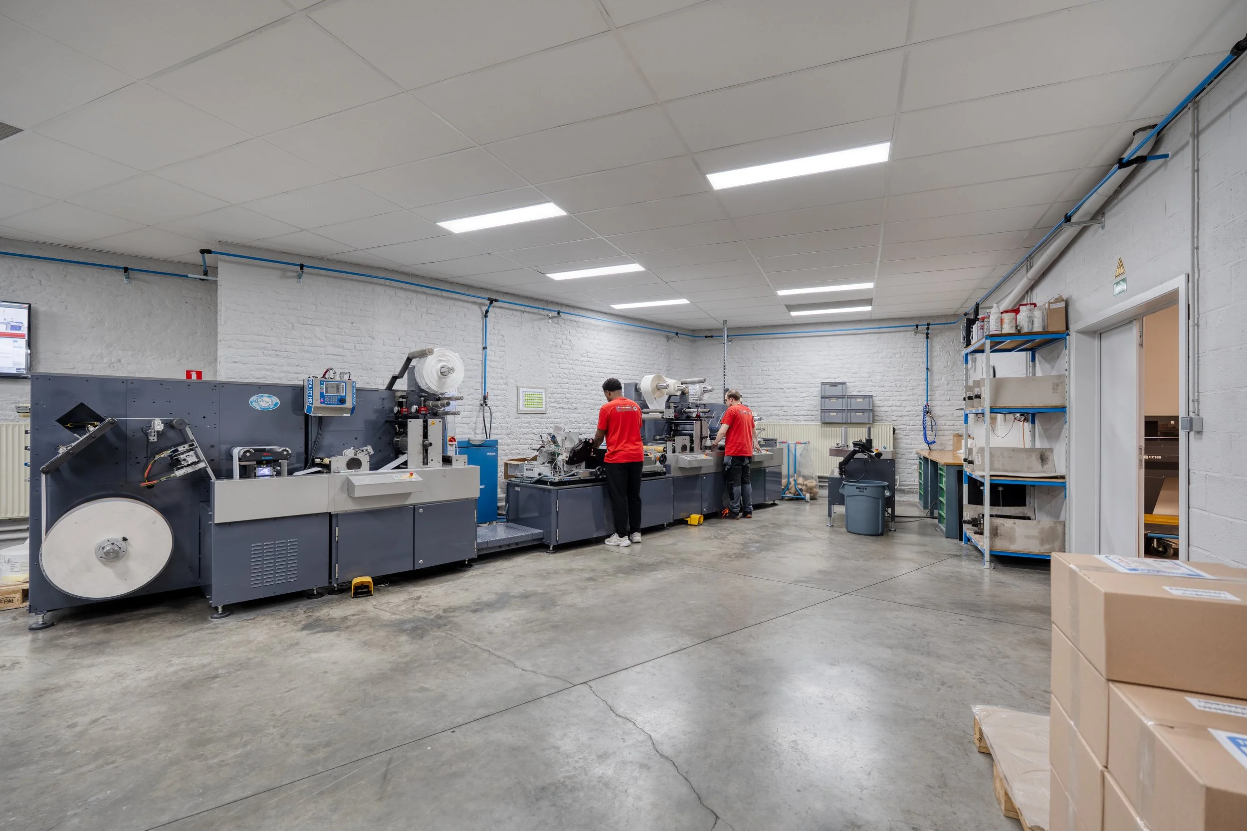 Une usine avec des machines industrielles et trois employés en uniformes rouges, travaillant dans une pièce bien éclairée et propre.