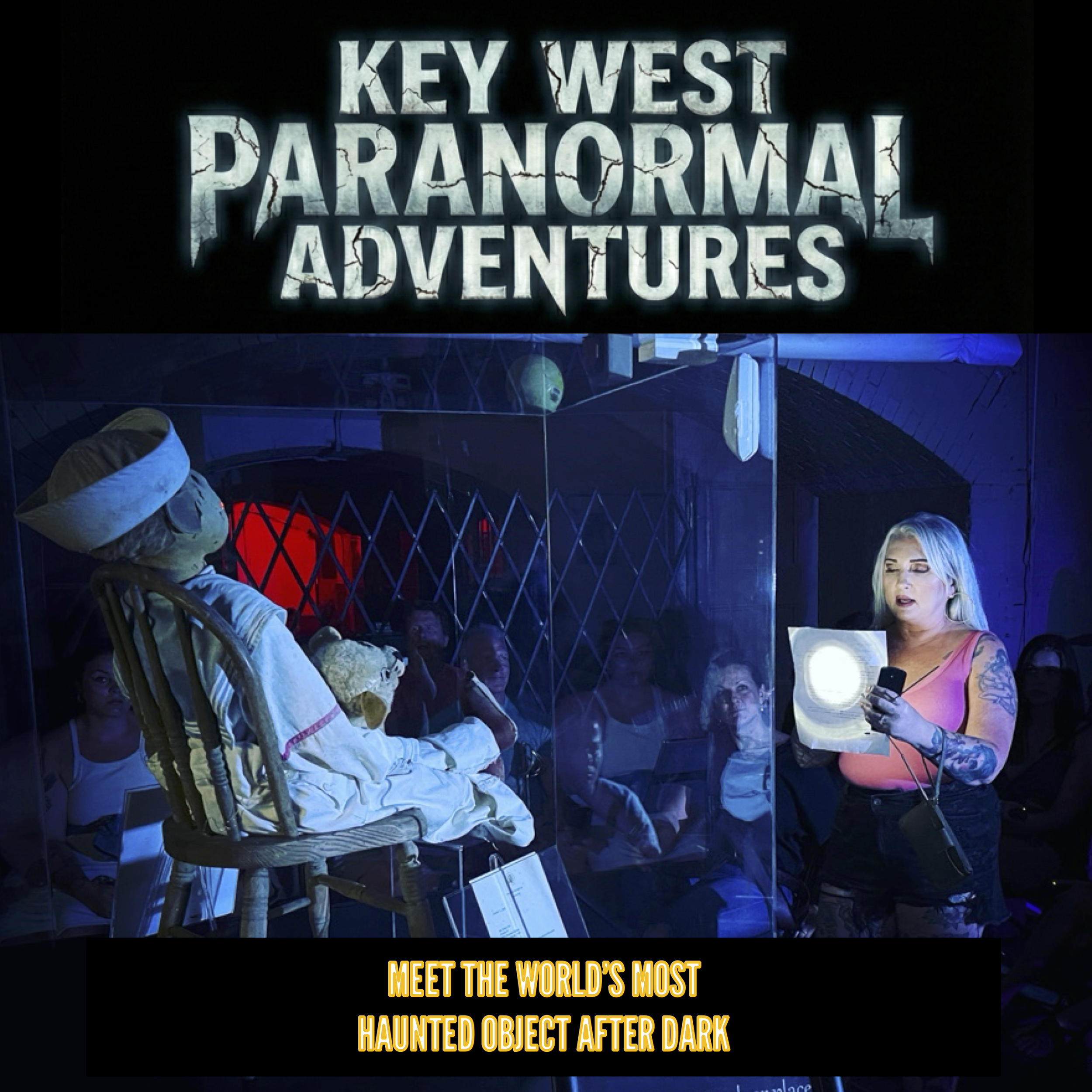 A woman with blonde hair and tattoos reading a guidebook at Key West Paranormal Adventures, with a person dressed as a ghostly character sitting nearby behind a glass display, in a dark, haunted setting.