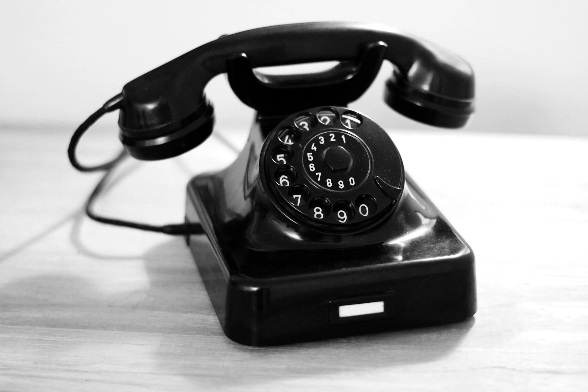 Black rotary dial telephone placed on a light-colored wooden surface.