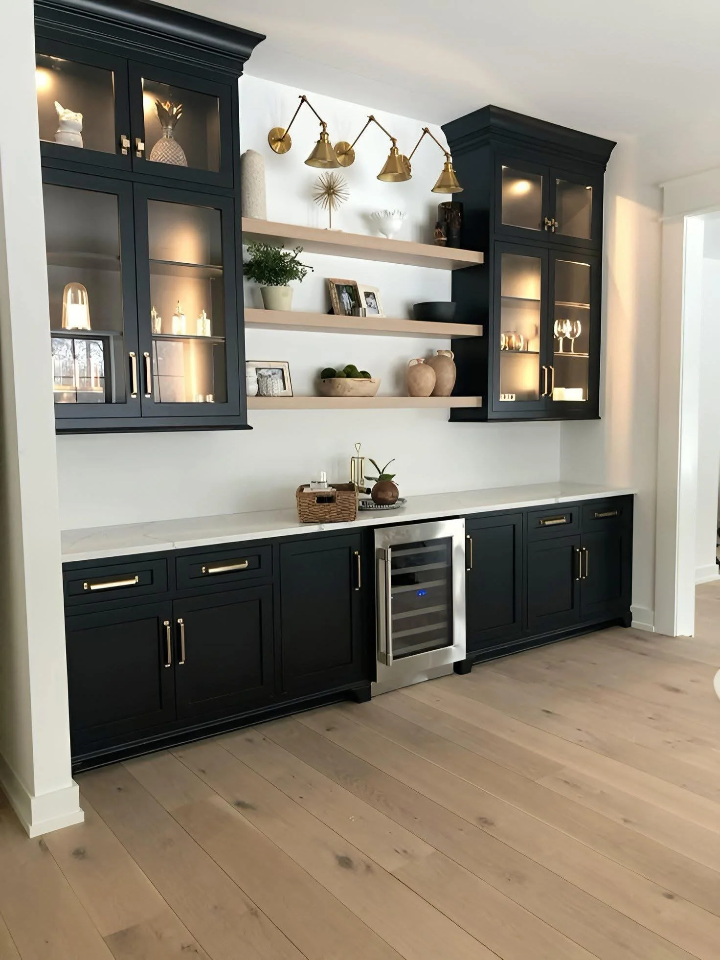 Kitchen bar area with dark blue cabinets, white marble countertop, and open shelves decorated with plants, picture frames, and decorative objects.
